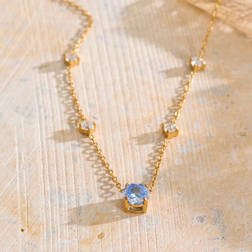 Shop the Bella Necklace: dainty gold station necklace with a blue zircon pendant. Waterproof, hypoallergenic stainless steel, adjustable.