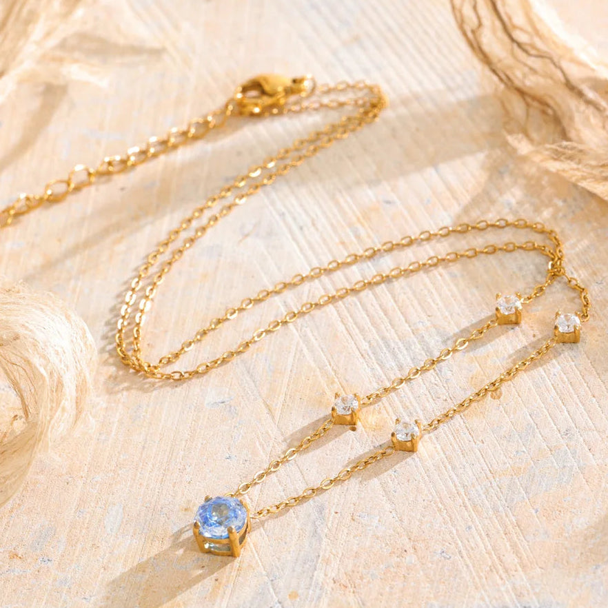 Shop the Bella Necklace: dainty gold station necklace with a blue zircon pendant. Waterproof, hypoallergenic stainless steel, adjustable.