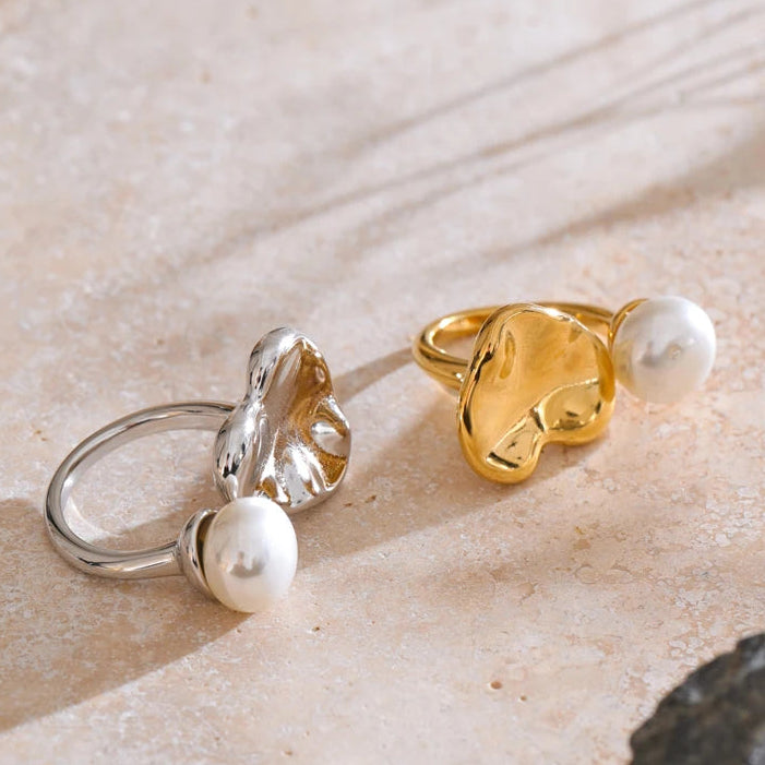Two pearl rings, one silver and one gold, on a textured stone surface.