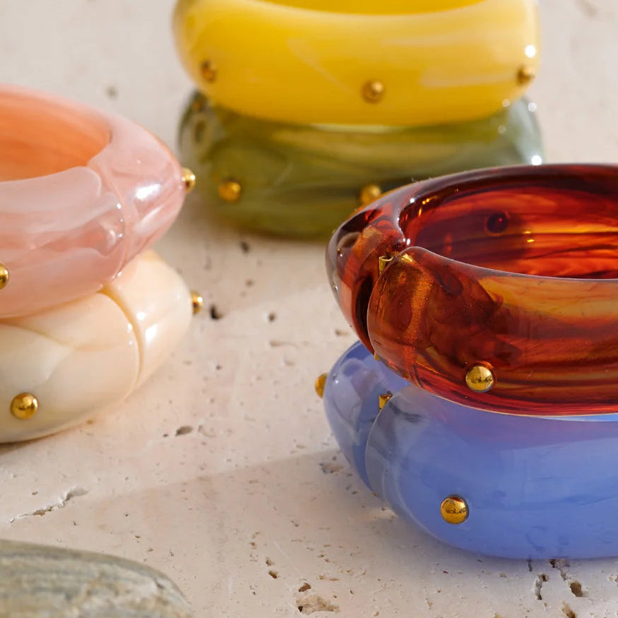 Colorful resin bangles with gold studs on a textured surface