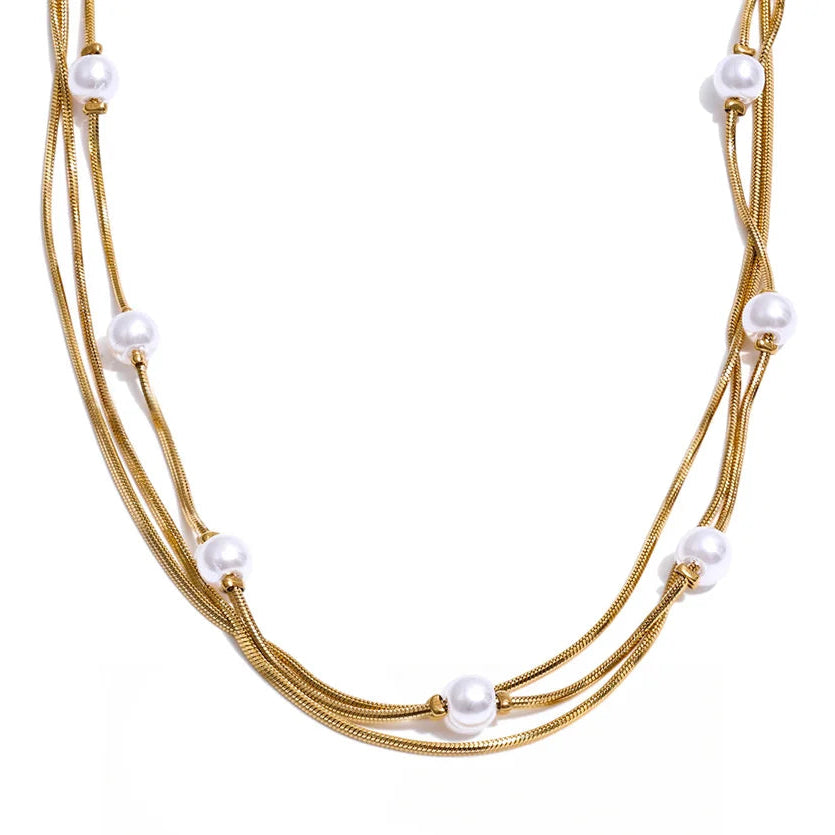 A multi-strand gold-tone snake chain necklace adorned with small white freshwater pearls, displayed against a clean white background with a black script logo at the bottom.