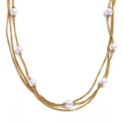 A multi-strand gold-tone snake chain necklace adorned with small white freshwater pearls, displayed against a clean white background with a black script logo at the bottom.