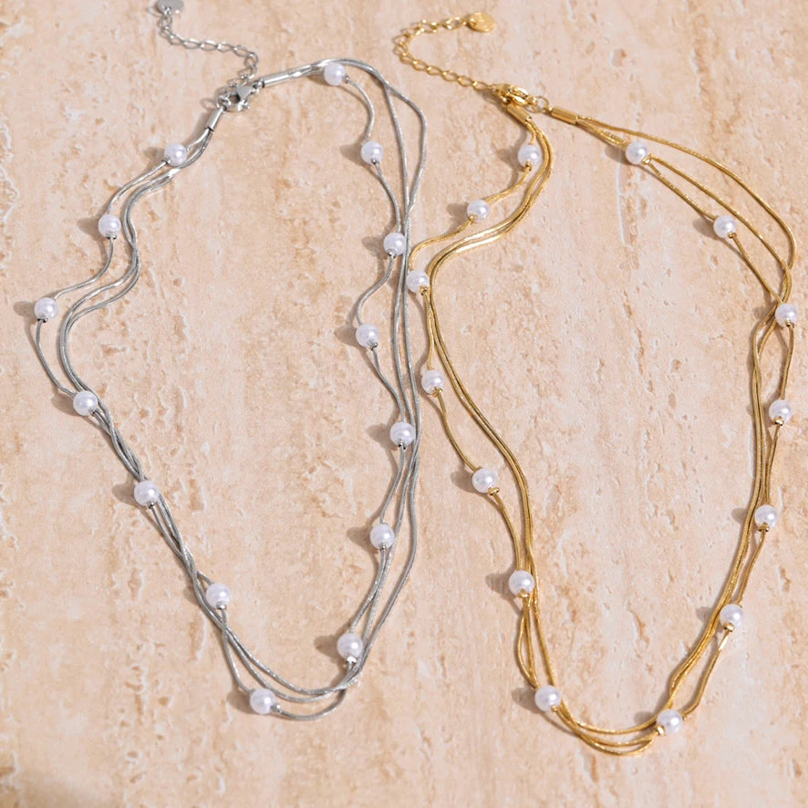 Two pearl necklaces, one gold and one silver, on a beige stone surface.