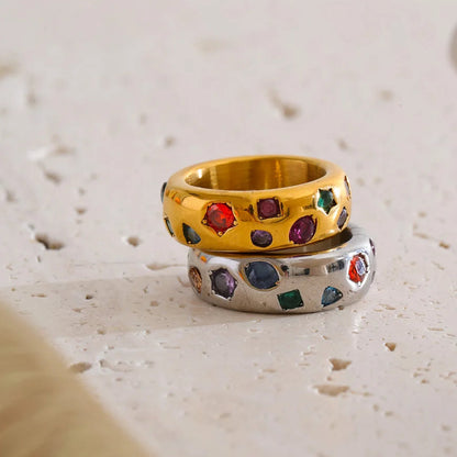 Two rings, one gold and one silver, with gemstones on a textured surface.
