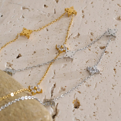 Two star-shaped necklaces, one gold and one silver, on a textured beige surface.