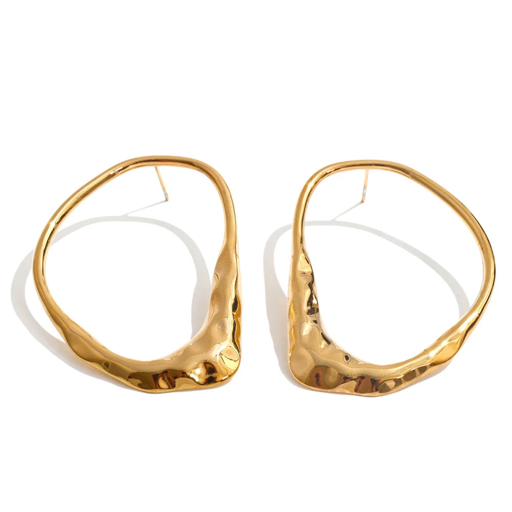 A pair of large, organic-shaped gold hoop earrings with a hammered texture, displayed on a clean white background.