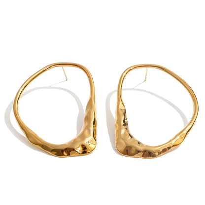 A pair of large, organic-shaped gold hoop earrings with a hammered texture, displayed on a clean white background.