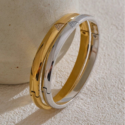 Gold and silver bangle on a textured beige surface. Waterproof stainless steel