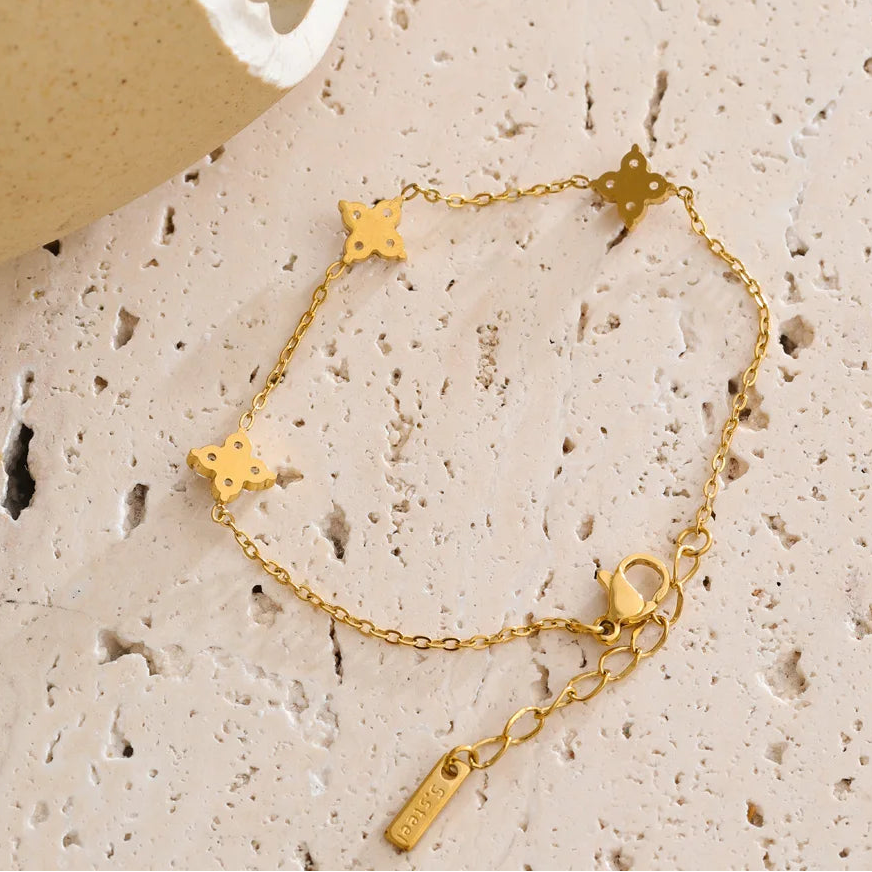 Gold bracelet with star-shaped charms on a textured beige surface