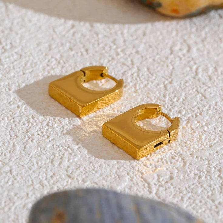 Gold hoop earrings on a textured white surface with a natural stone background