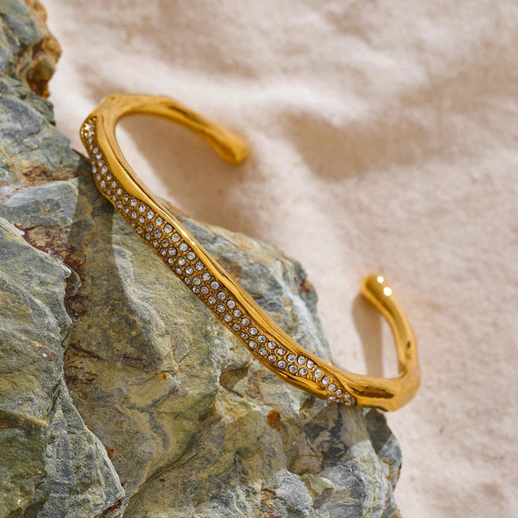 Gold bracelet with embedded stones on a textured stone surface