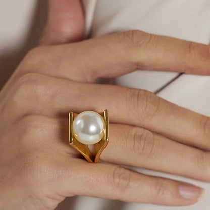 Gold ring with a pearl on a hand against a neutral background
