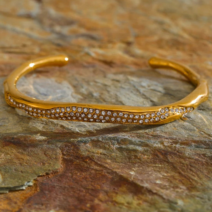 Gold bracelet with embedded stones on a stone surface