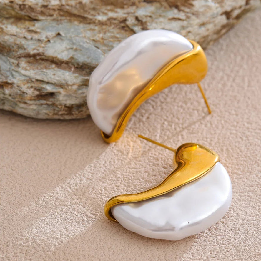 Gold and white earrings on a textured surface