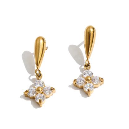 A pair of gold drop earrings with teardrop-shaped posts and flower-shaped dangles set with clear round gemstones, shown on a white background with soft shadows.