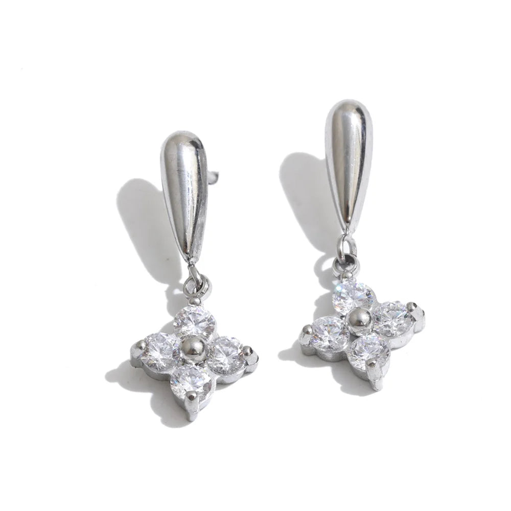 A pair of silver-toned drop earrings with teardrop-shaped hooks and four-prong flower charms set with clear stones, shown on a white background with soft shadows.