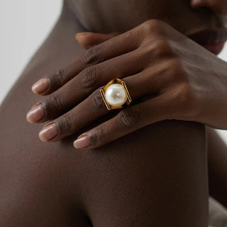 Woman wearing a gold ring with a pearl on a neutral background