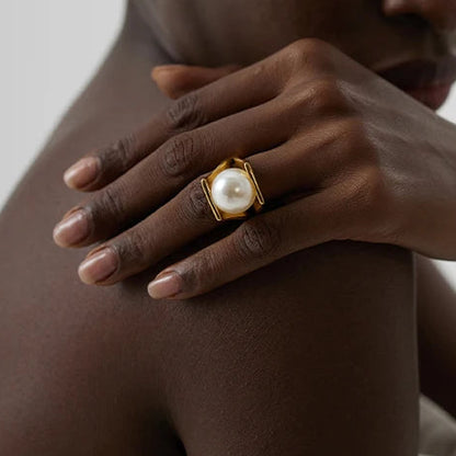Woman wearing a gold ring with a pearl on a neutral background