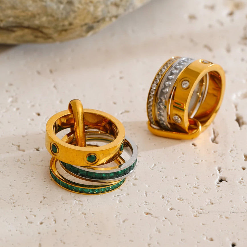 Gold and green rings on a textured surface with a stone and leaf in the background