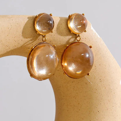 Pair of earrings with large round stones on a beige stone surface