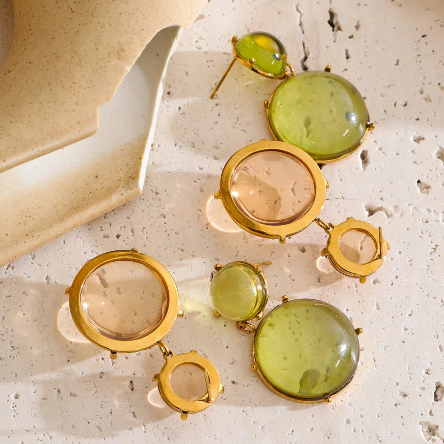 Gold and green earrings on a textured surface