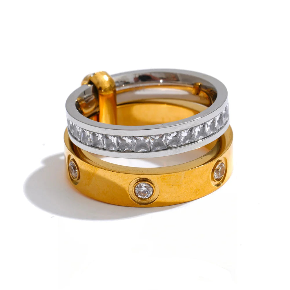 A stack of two rings on a white background: a gold band with small clear stone accents and a silver-toned band with a row of clear stones, with a gold clasp visible on the top ring