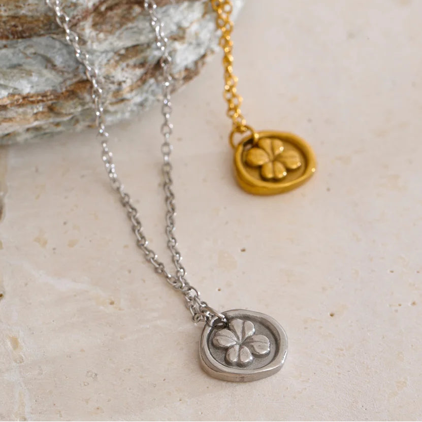 Two necklaces with clover pendants on a stone surface