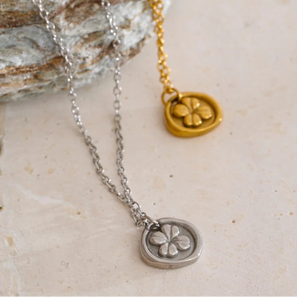 Two necklaces with clover pendants on a stone surface