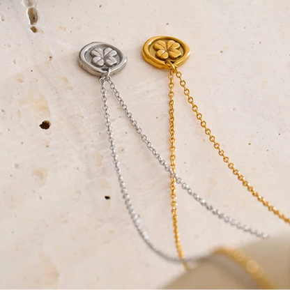 Two gold and silver necklaces with clover designs on a textured beige
surface. Waterproof stainless steel