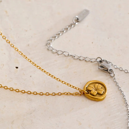 Gold necklace with a clover-shaped pendant on a beige background