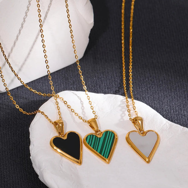 Three heart-shaped pendants on gold chains displayed on a white stone surface.
