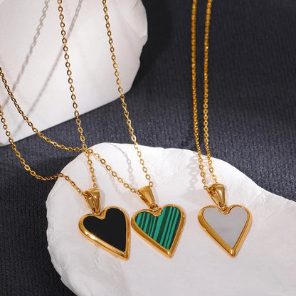 Three heart-shaped pendants on gold chains displayed on a white stone surface.