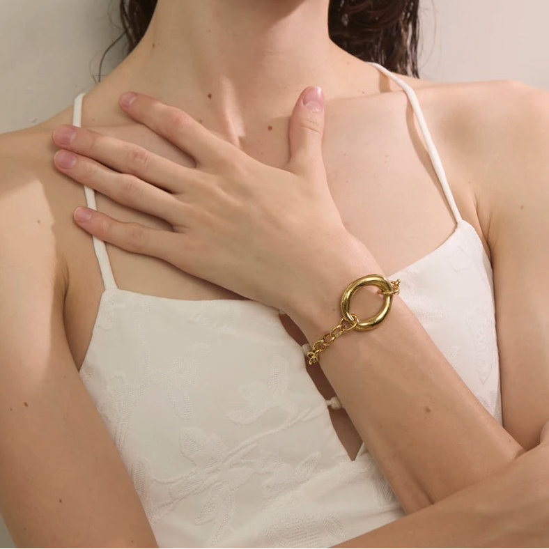 Woman wearing a gold bracelet on her wrist, with a neutral background