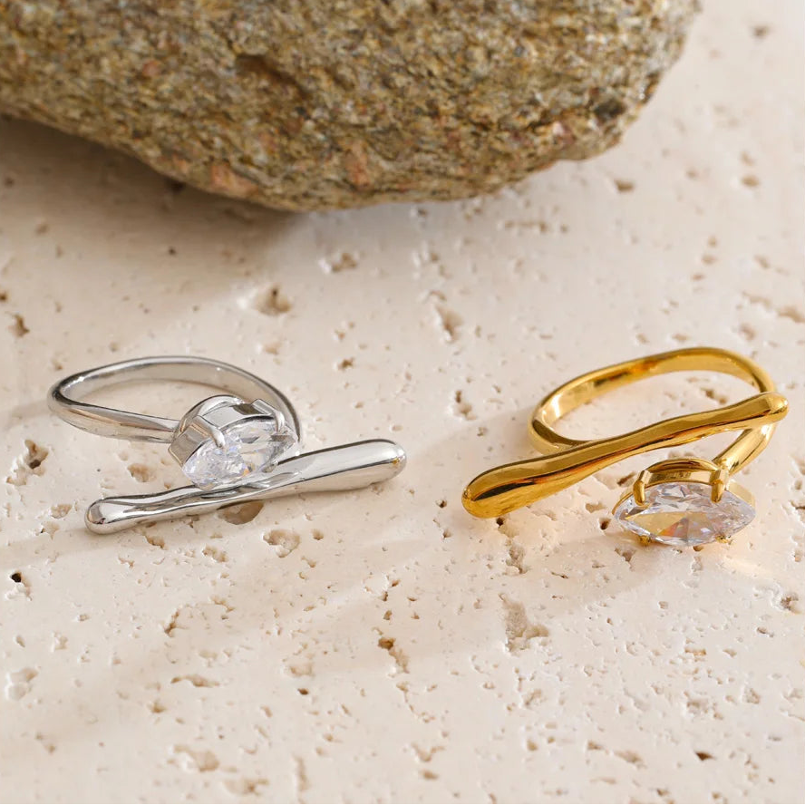 Two rings, one silver and one gold, on a textured surface with a rock in the background.