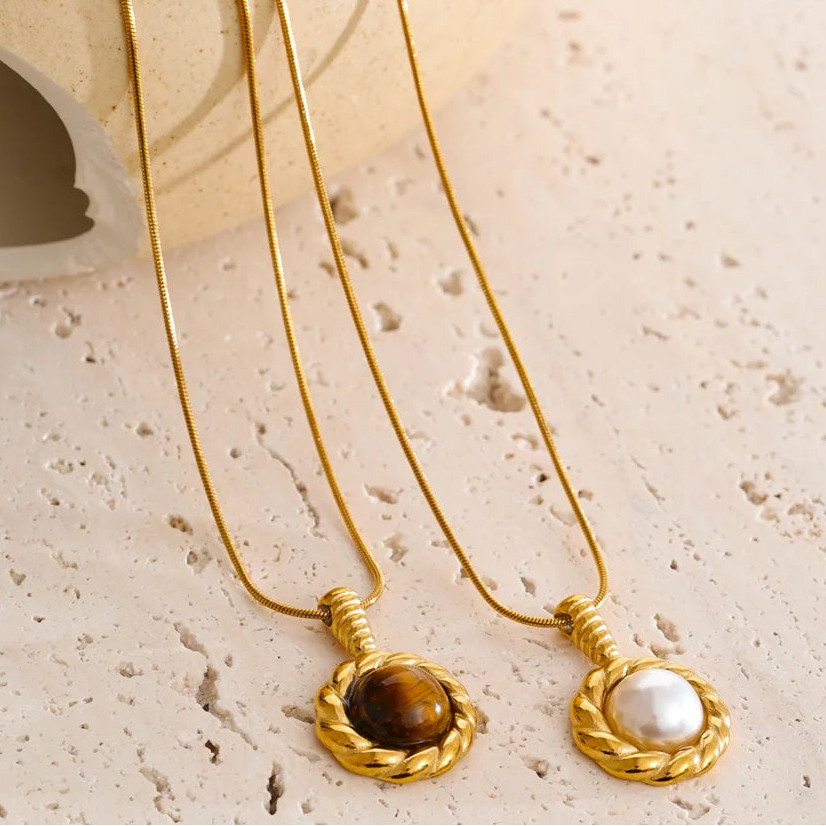 Two gold necklaces with gemstone pendants on a textured beige surface