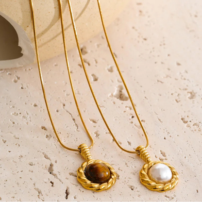 Two gold necklaces with gemstone pendants on a textured beige surface