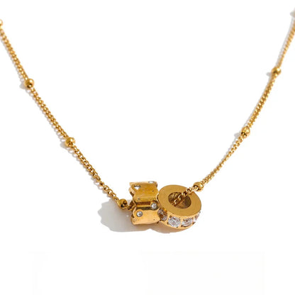A gold chain necklace featuring a small gold charm with a circular letter 'O' design, accented with clear rhinestones, displayed on a clean white background with a black script logo at the bottom.