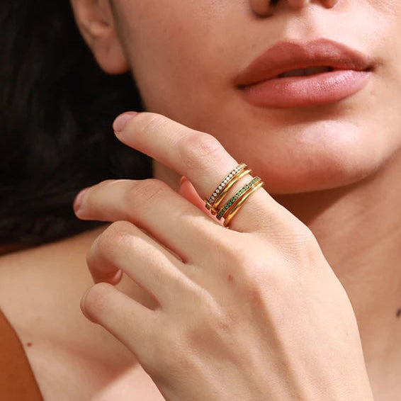 Close-up of a woman wearing a gold ring on her finger, with a neutral background.