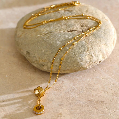 A gold chain necklace with a small round pendant and a faceted gold cube charm, stainless steel
