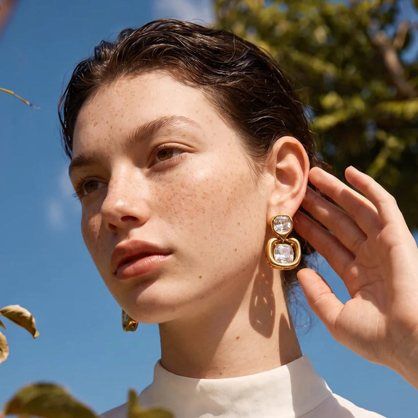 Shop the Sophie Earrings: modern drop studs with stacked cushion-cut zircons. Waterproof, hypoallergenic stainless steel in 18k gold-tone.