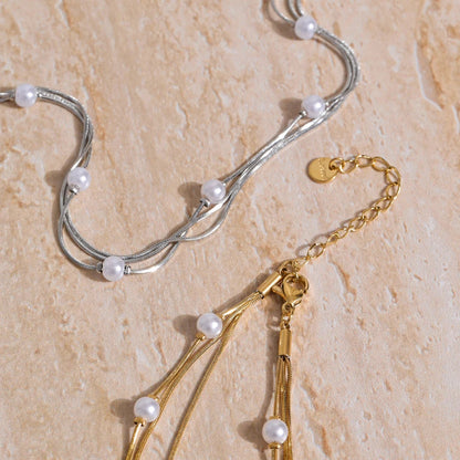 Two necklaces, one gold and one silver, with pearl beads on a beige stone surface.