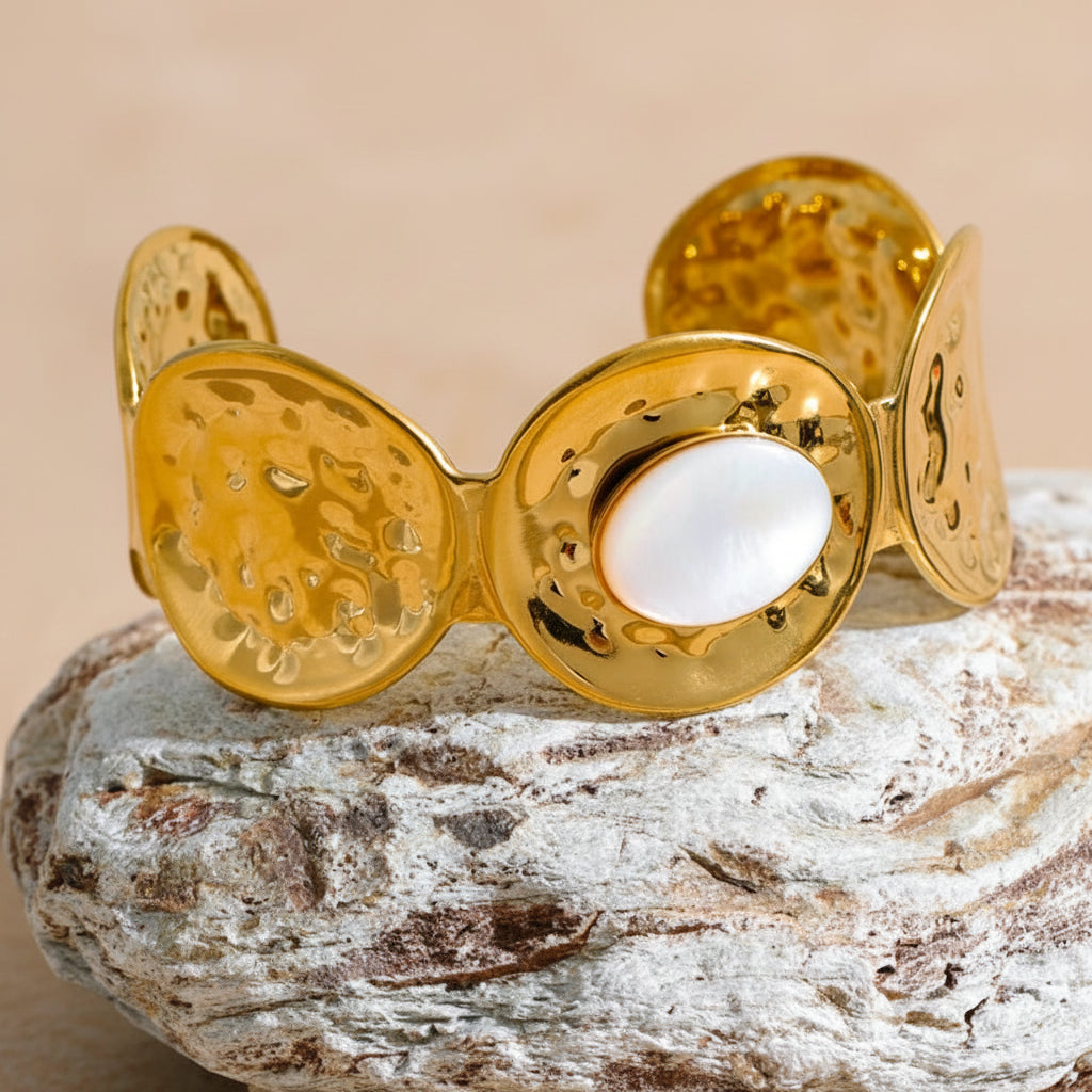 Gold bracelet with a central white stone on a textured surface with green foliage in the background