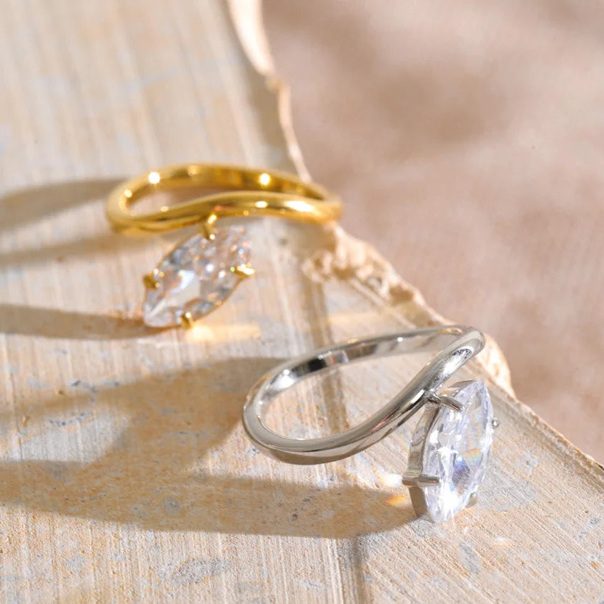Two marquise-cut gemstone rings, one in yellow gold and one in silver, displayed on a textured beige stone surface. stainless steel