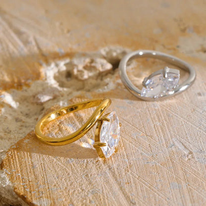 Two marquise-cut gemstone rings displayed on a textured beige stone surface. One ring features a polished yellow gold band, and the other features a silver-toned band.