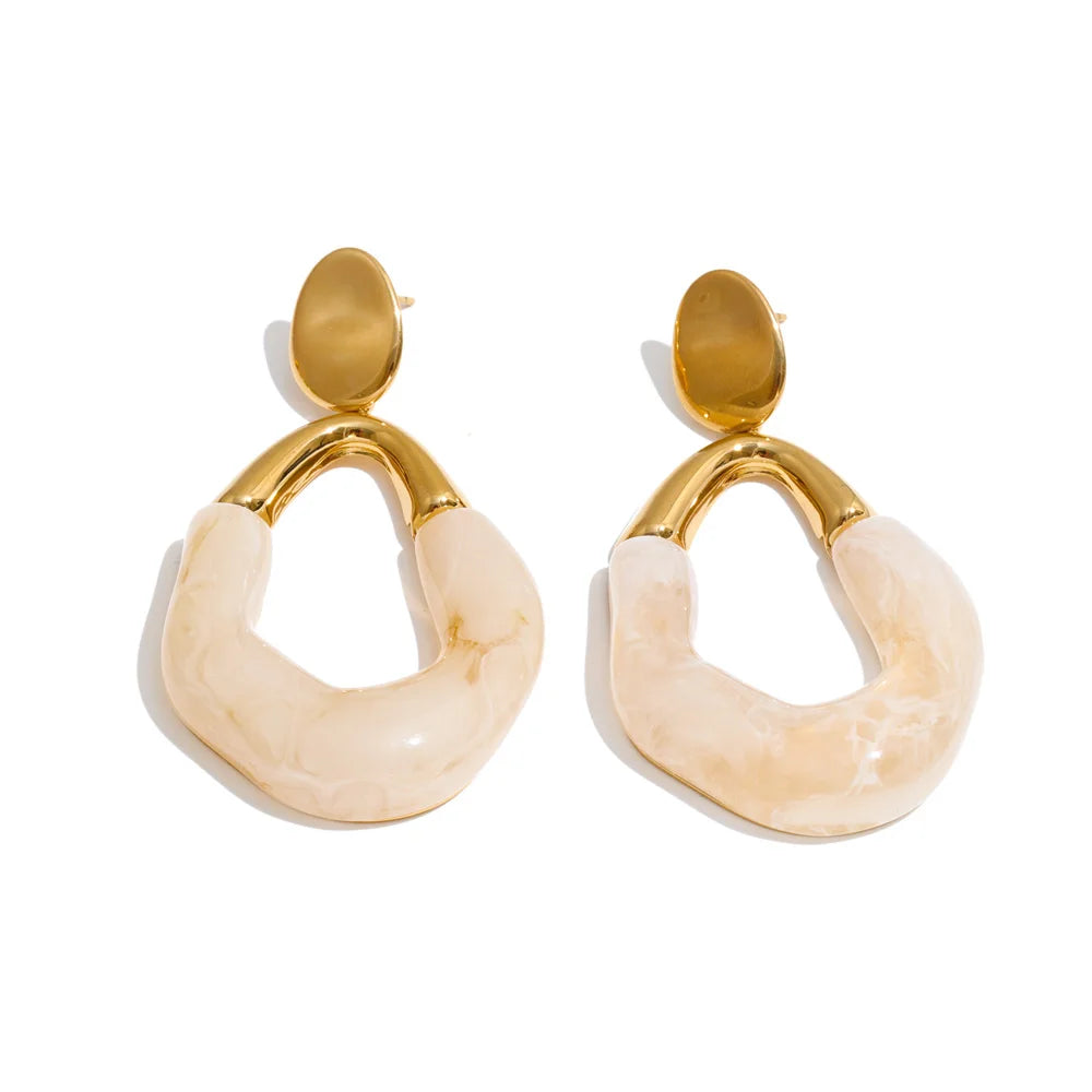 A pair of gold and cream-colored drop earrings with a polished gold oval post and a curved cream stone pendant, shown on a white background. Stainless steel statement earrings