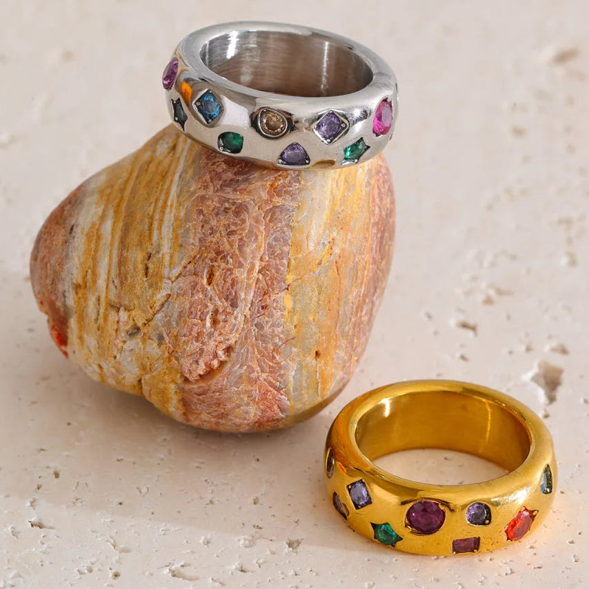 Silver and gold rings with colorful gemstones on a stone surface