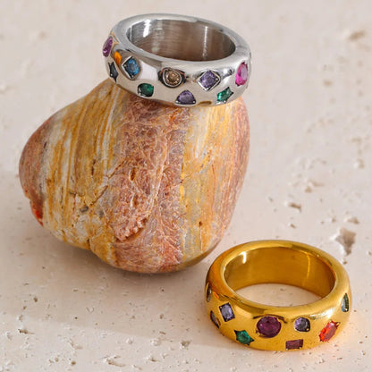 Silver and gold rings with colorful gemstones on a stone surface