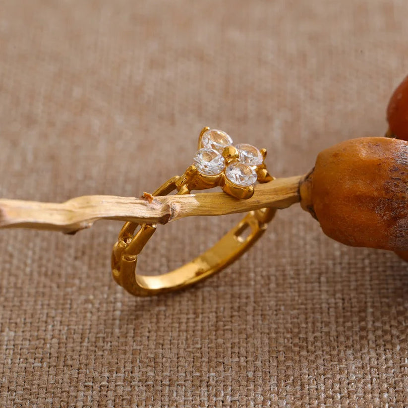Gold ring with diamante accents on a wooden stick against a textured brown background