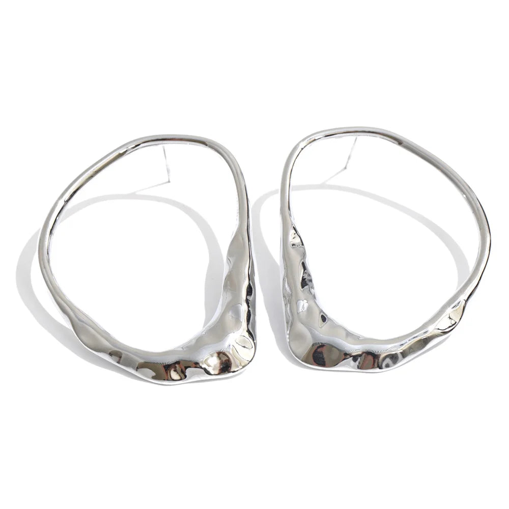 A pair of large, organic-shaped silver hoop earrings with a hammered, textured finish, displayed on a clean white background.