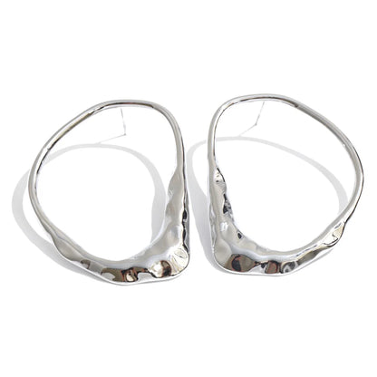A pair of large, organic-shaped silver hoop earrings with a hammered, textured finish, displayed on a clean white background.